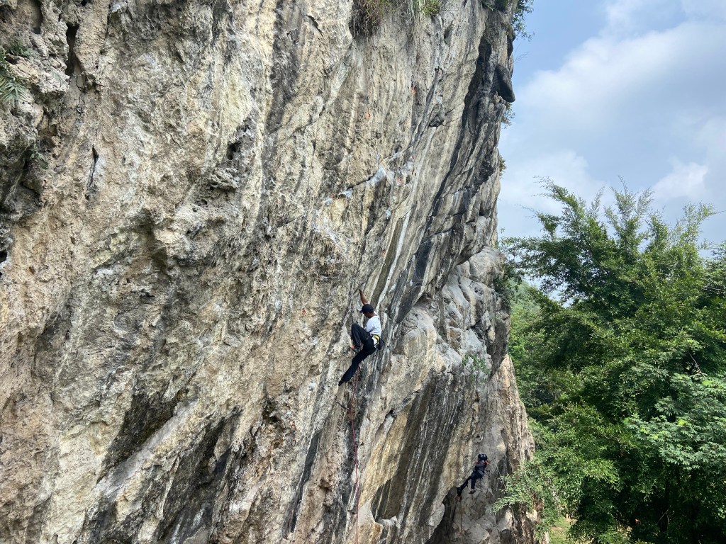 Climber on overhanging limestone wall at Citatah. The limestone is white with large grey and black stripes running down the wall. 