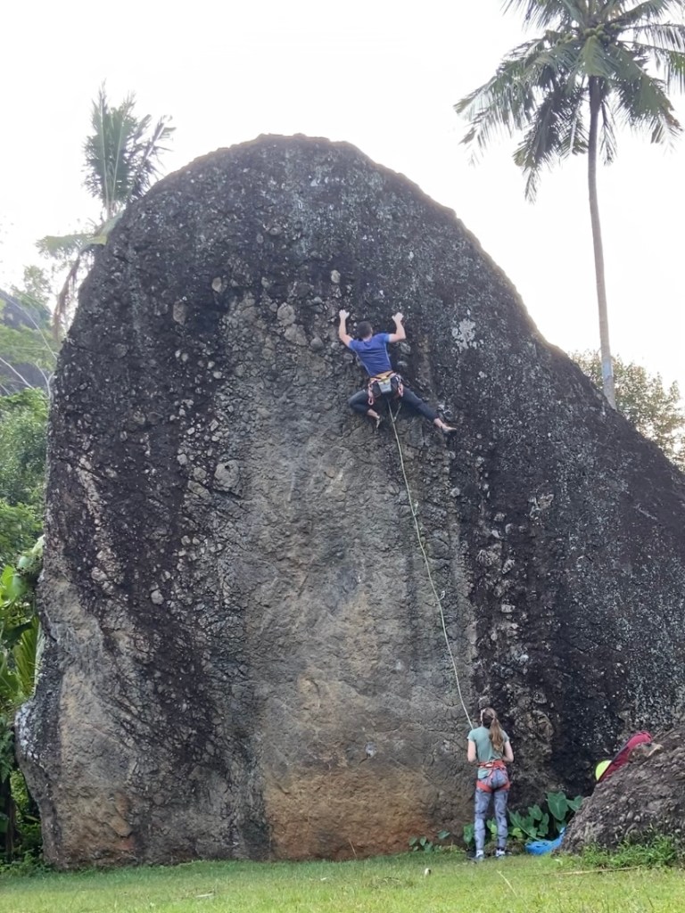 Climber on large black and grey boulder using large pebbles protruding from the wall .