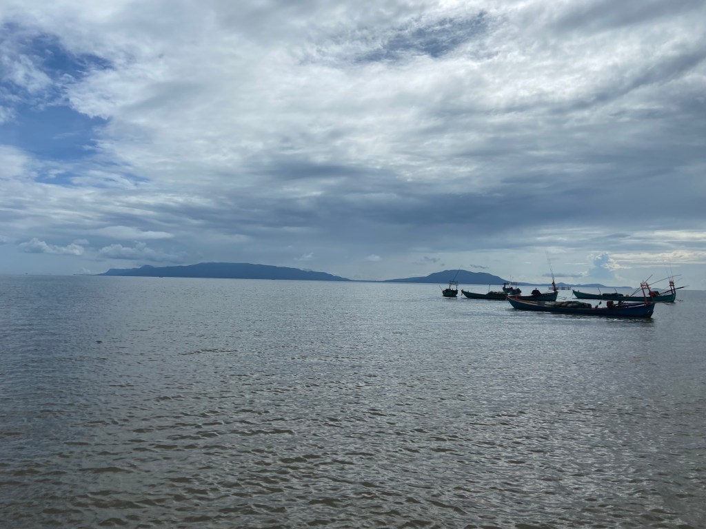 Wooden fishing boats on the Gulf of Thailand with the Vietnamese island of Phú Quốc in the background on a cloudy day.