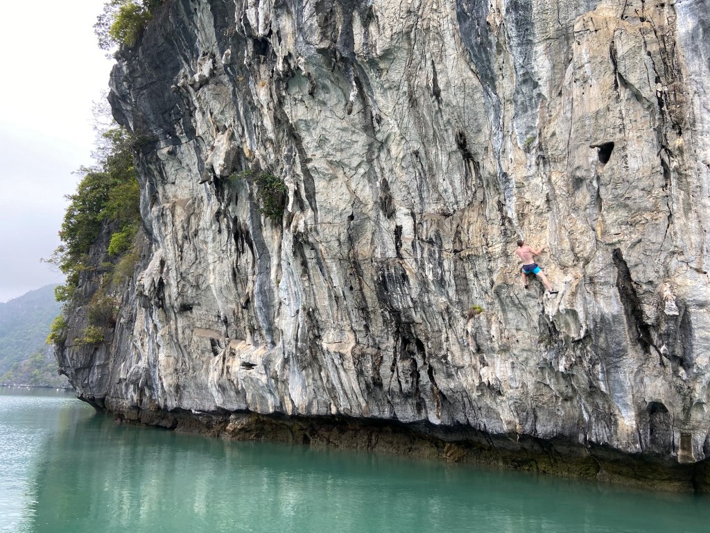 Climber looking upwards for the next move high up on the limestone wall above the sea. The begin of the wall is steep and undercut. 