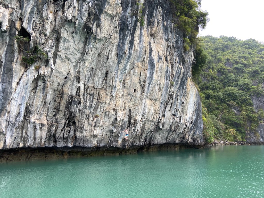 Climber free falling into the sea after deep water soloing on white limestone cliff