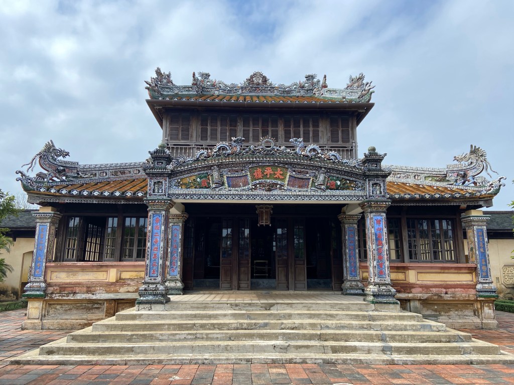 Ornately decorated front of a building located in the Citadel of Huế. It has Chinese writing above the entrance and down the pillars.  