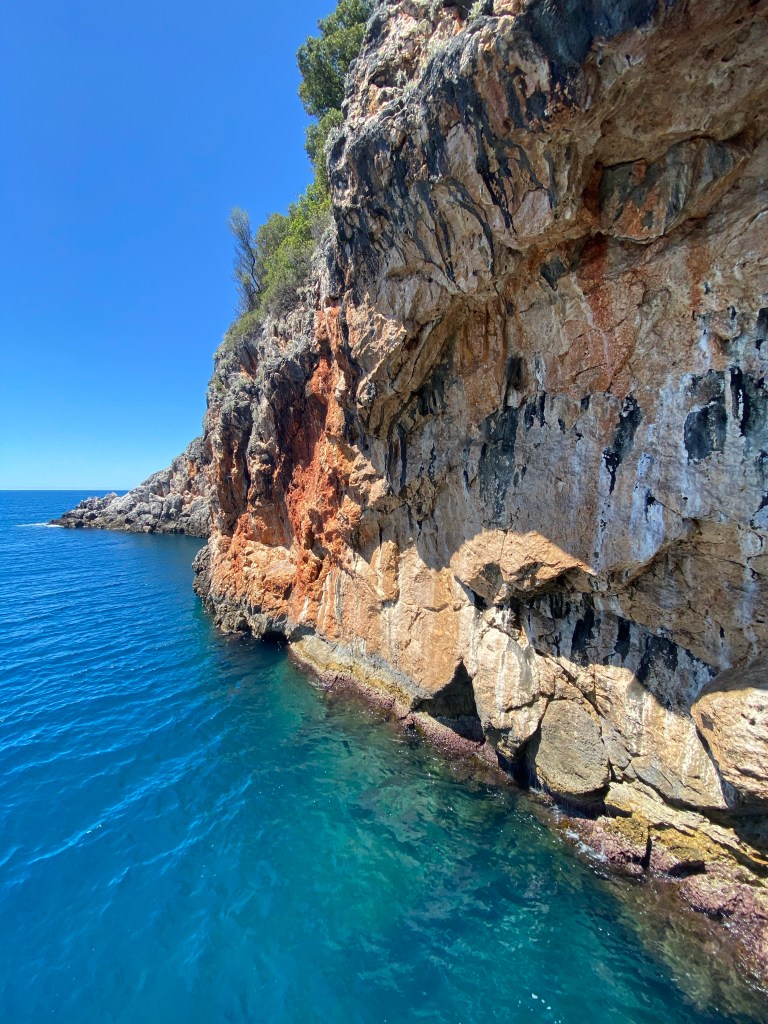 Red ish limestone crag above clear deep water water 