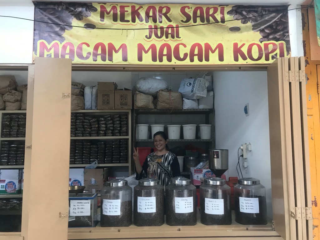 Smiling woman behind her stall of large containers filled with a variety of different coffee beans from the region. 