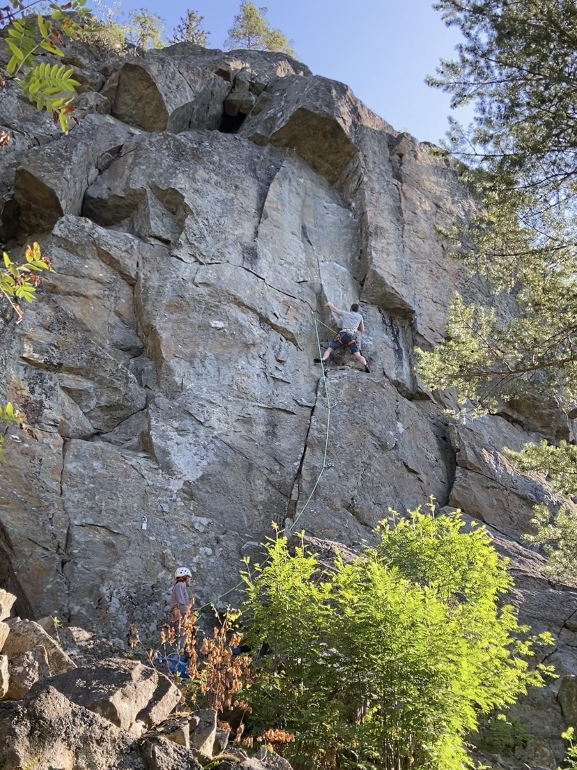 Climber using a left hand side pull and using their balance on the featured crag of Midskogsberget