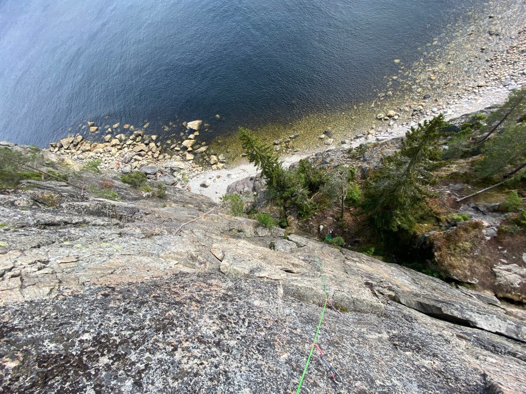 Looking down the granite cliff to the pine forest, rocky beach and sea below