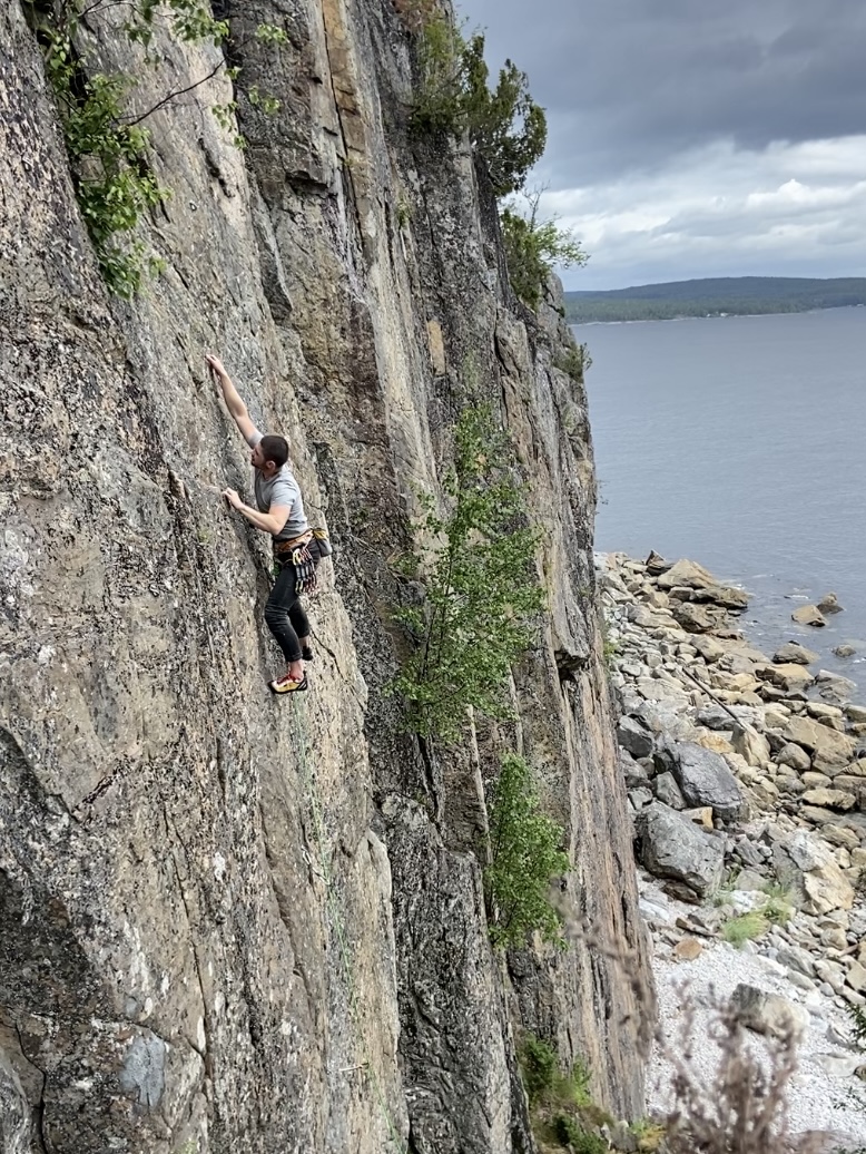 Climber reaching for high crimps on the grey compact slab above the rocky beach
