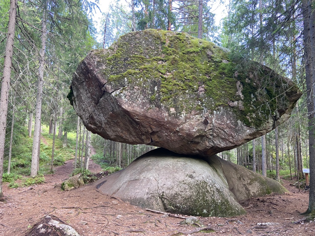 Large granite boulder balanced on a piece of bedrock in the forest 