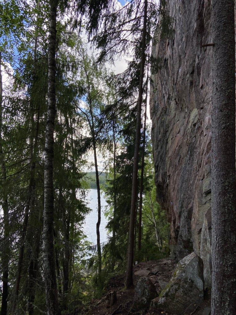 Pink and grey granite wall within the forest with a lake at the base of the crag