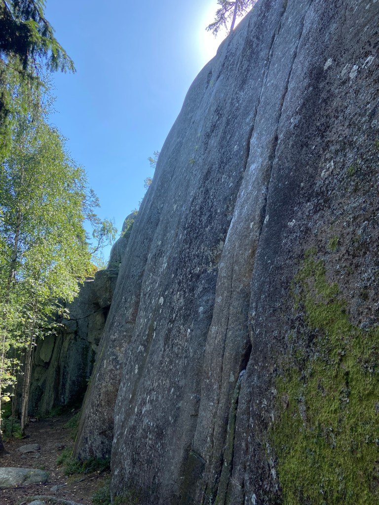 Granite outcrop in the forest with vertical crack features which the climbs follow with blue sky 