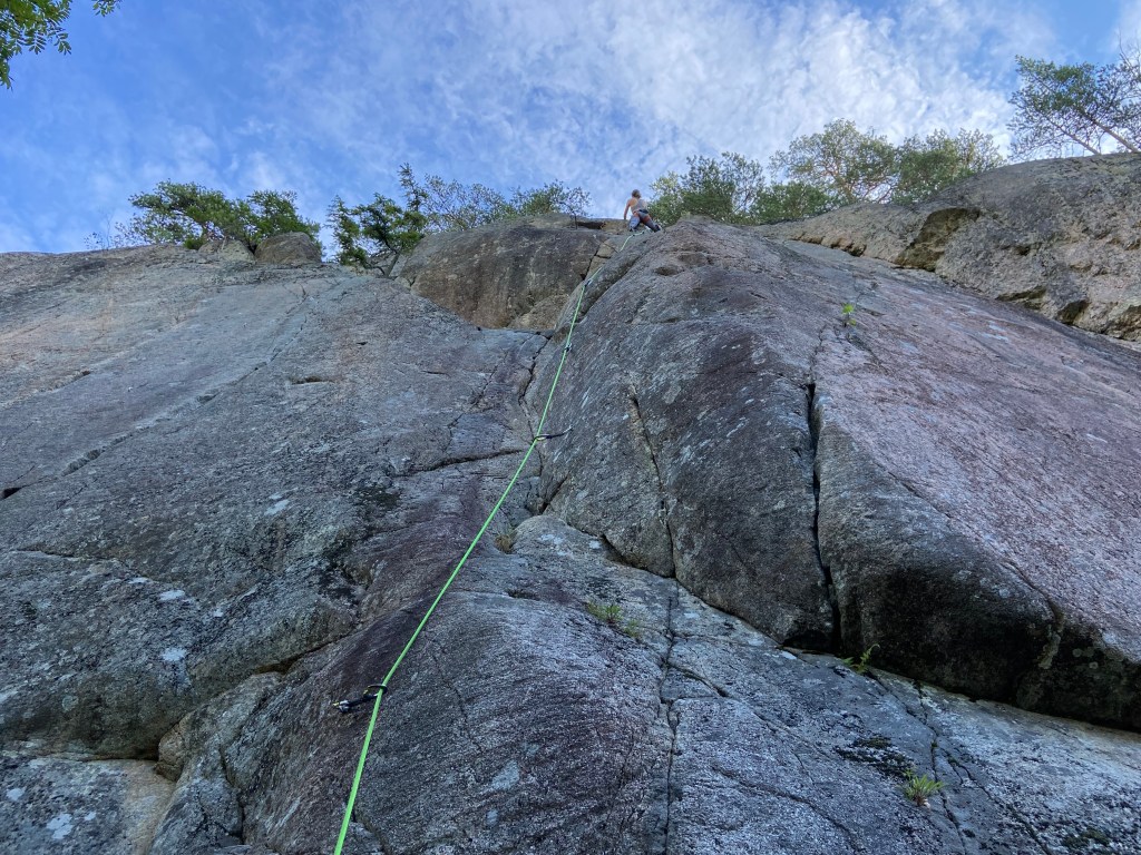 Climber on a slightly overhanging grey granite crag looking up for the next moves