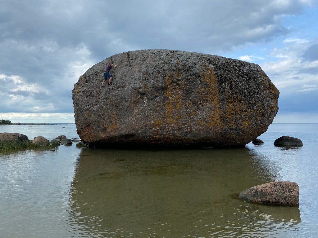 Climber traversing high up on a huge boulder which is submerged at the base with the tide