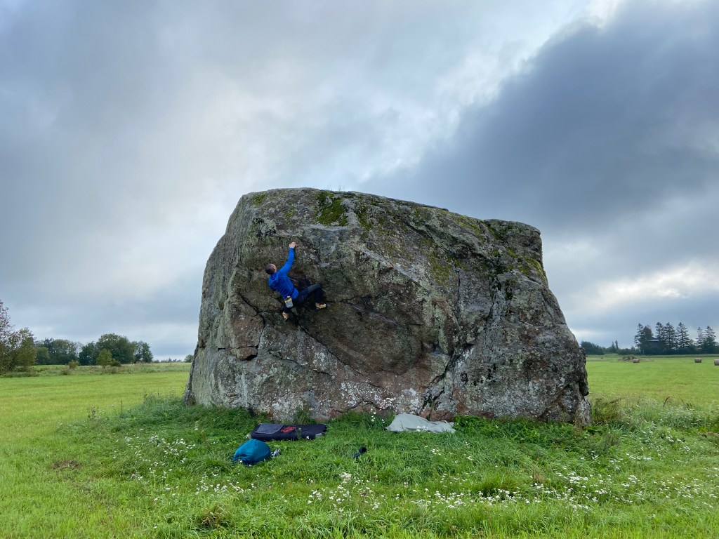 Climber tackling the overhanging part of the boulder set within a field on a moody and cloudy day