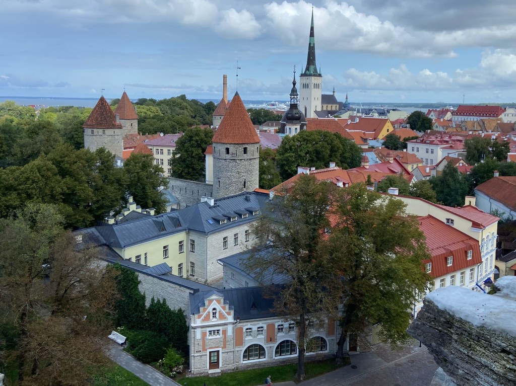 Looking out towards the sea over the tops of old stone turrets and pastel old town houses with orange and black roofs. 