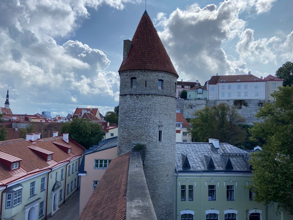 Old stone tower with small windows rising up from the pastel colour townhouses on the cobble road beneath 