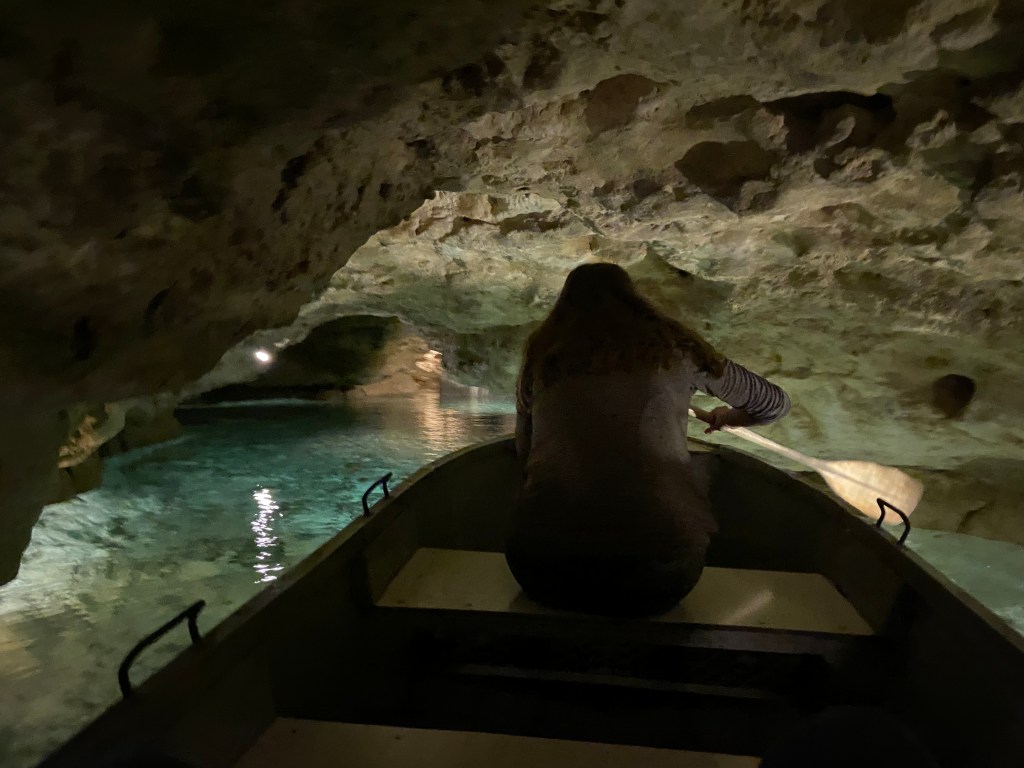 Person in a boat with a paddle making their way through a narrow passage way within a cave with crystal thermal water flowing through it. 