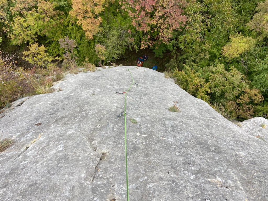 View down towards the belayer which shows the blankness of the slab. The grey limestone is featureless. 