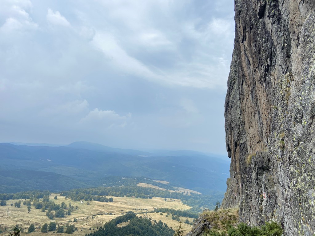 Volcanic rock which is grey to yellow in colour soaring high above the mountain plains below. The crag overlooks different hills, patches of forest and pastures. 