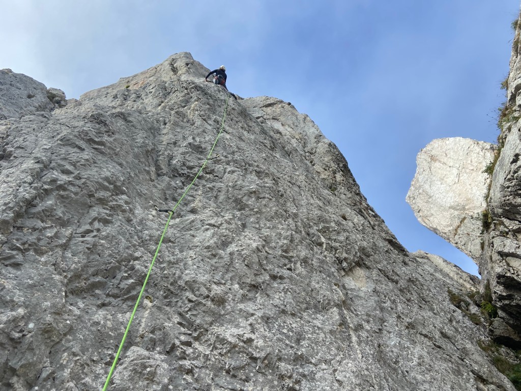 Climber on a vertical white limestone section of rock which is surrounded by other limestone pinnacles. 