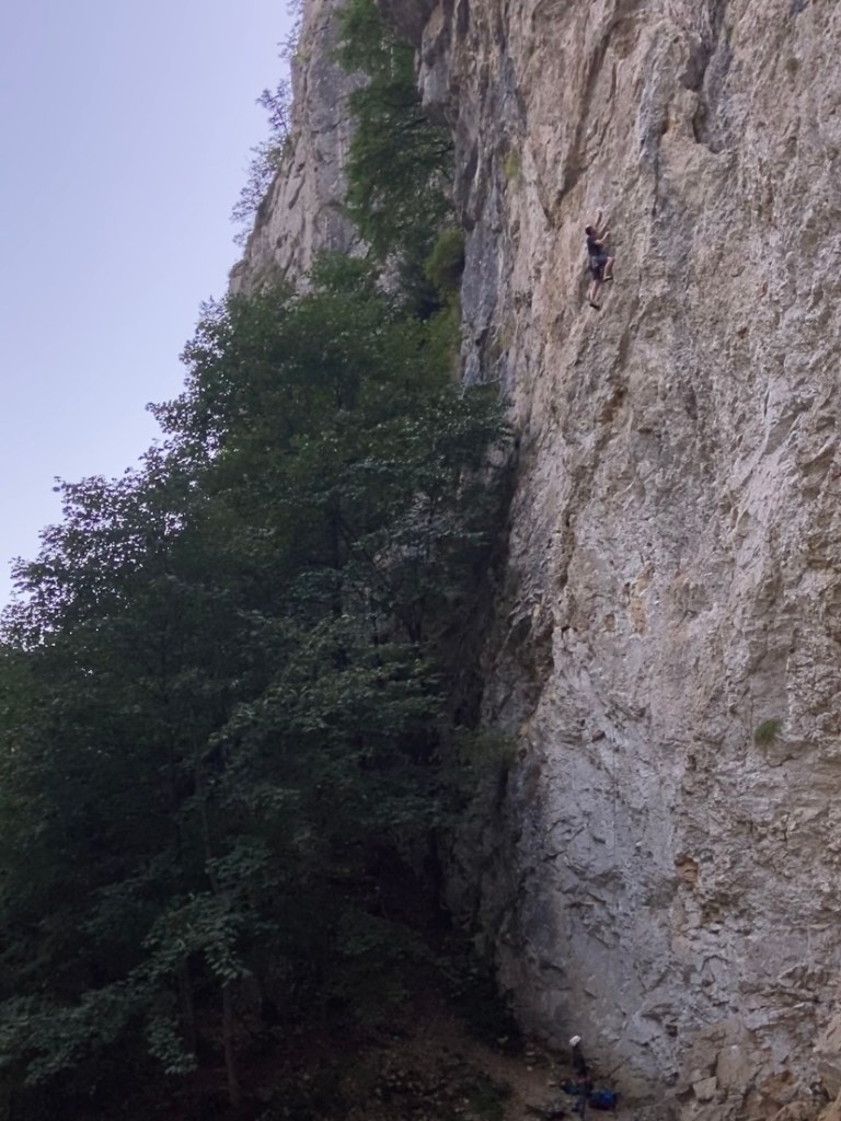 Climber around 25 meters high on limestone wall climb reaching up to make the next hand move. 