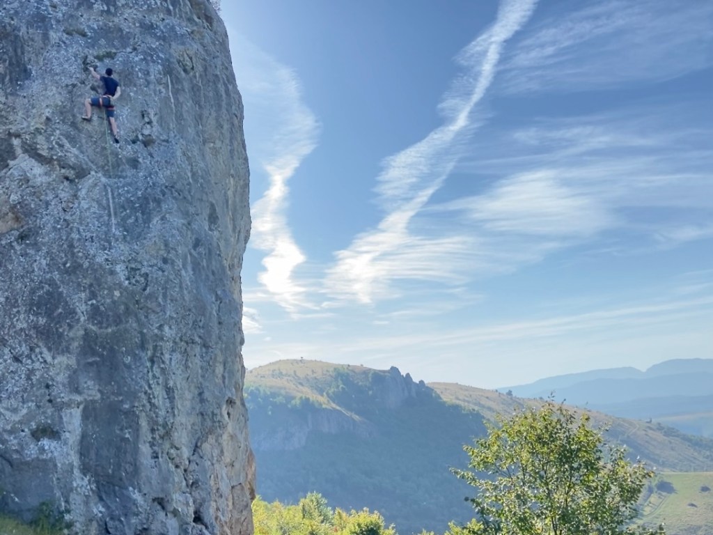 Climber chalking up looking for the next handhold. The rock is a grey vertical limestone overlooking more grassy mountains. 