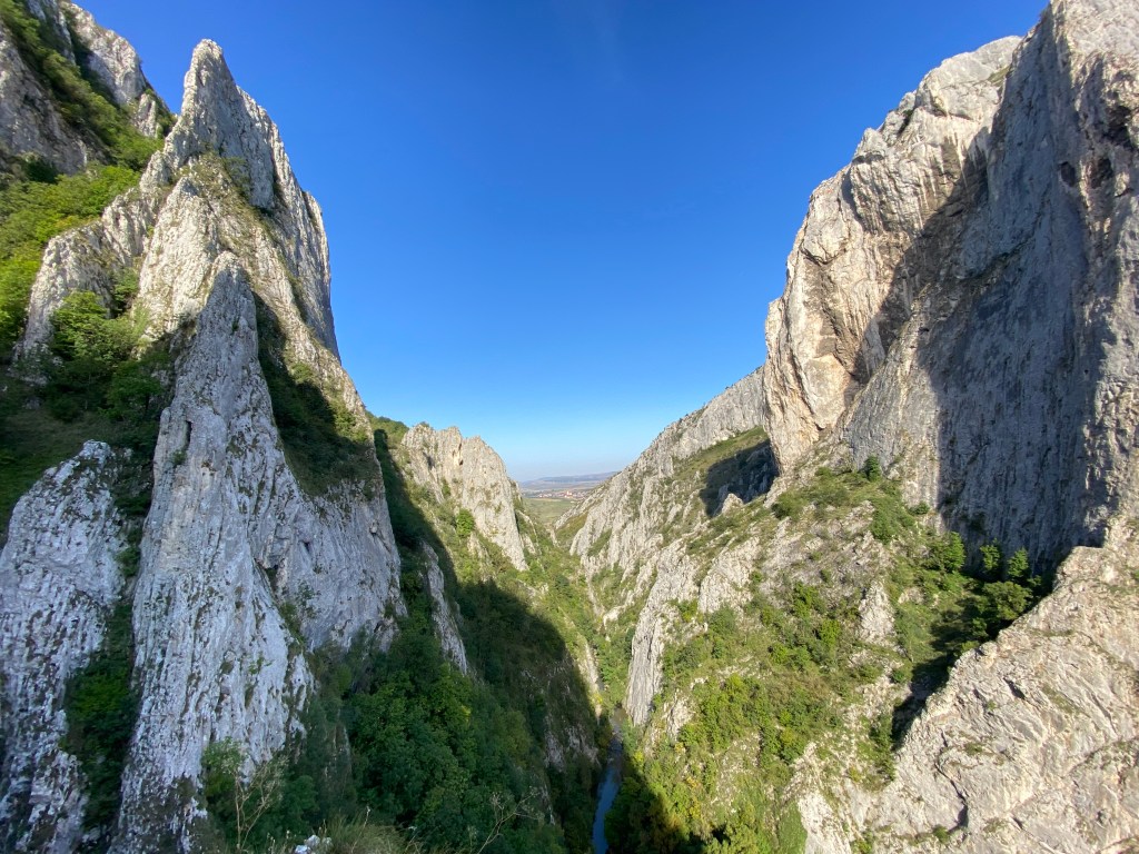view looking down towards the end of the narrow gorge. There are rocky walls on both sides with trees among the gaps. At the bottom of the gorge flows a bright blue river. 