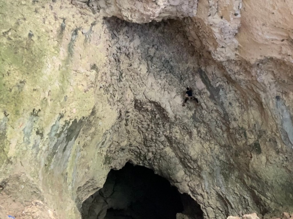 Climber lost among a sea of steep grey rock in a deep and tall cave 