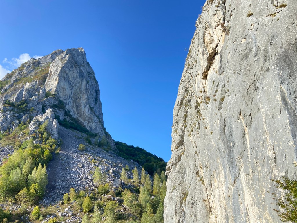 Looking across from a smooth limestone wall to a giant pointed mountain face in the distance. 