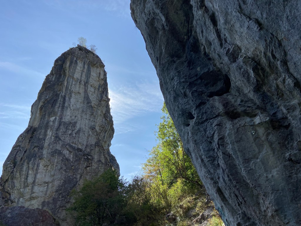 Tall limestone pinnacle with a large and imposing wall on one side with white and grey/blue streaks running down it. there is also another, steeper limestone wall to the right of it. 