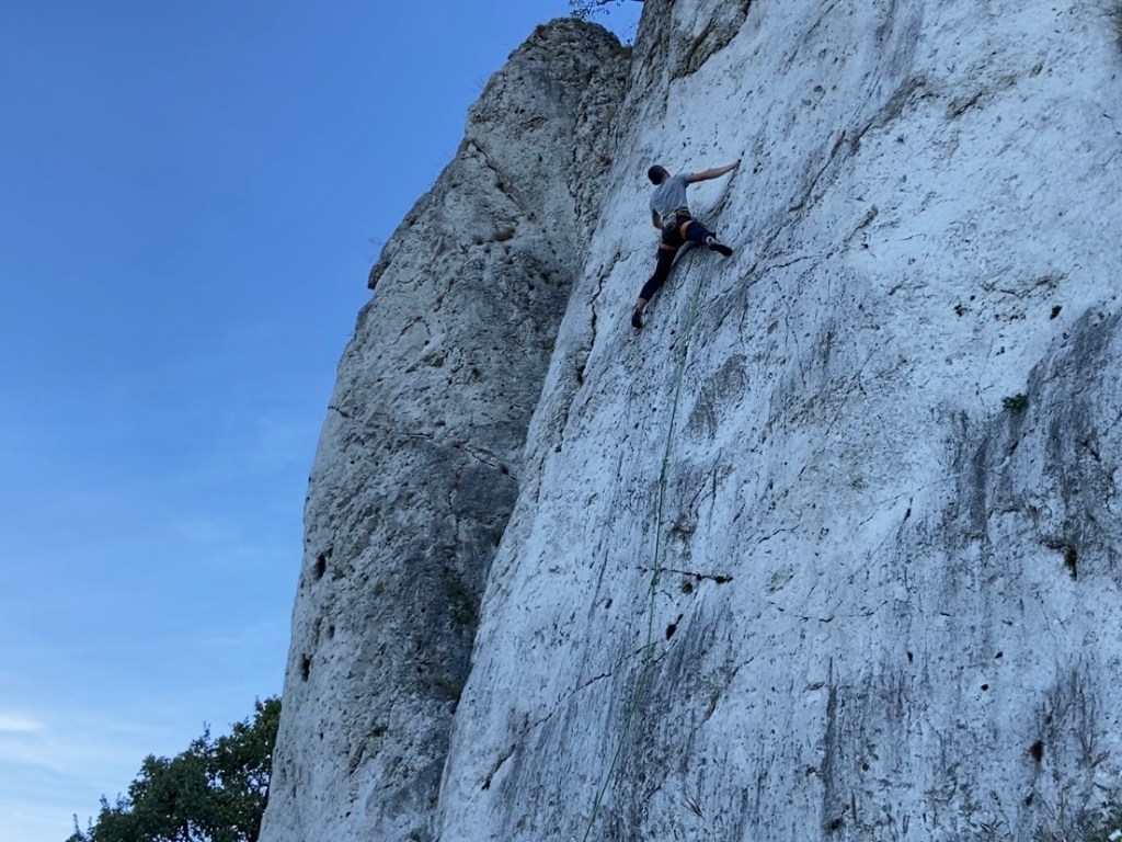 Climber on stark white limestone which is pocketed and features some diagonal and horizontal scratch like cracks on the rocks. 