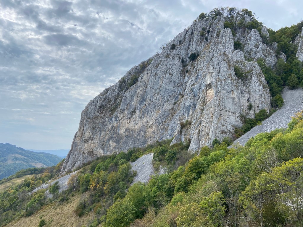 Volcano shaped limestone cliff on the top of a high mountain surrounded by trees and scree. 