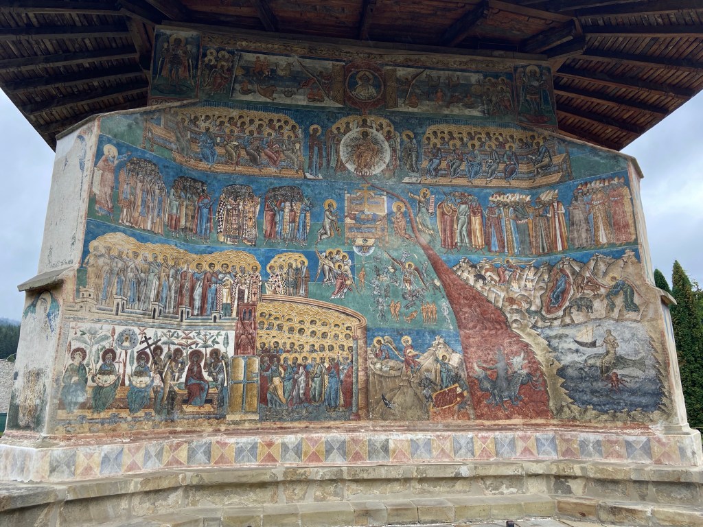 Ancient fresco of judgement day on the outside wall of an Orthodox Church. It depicts many different characters, animals and scenes relating to bible stories.  It is under a wooden roof.