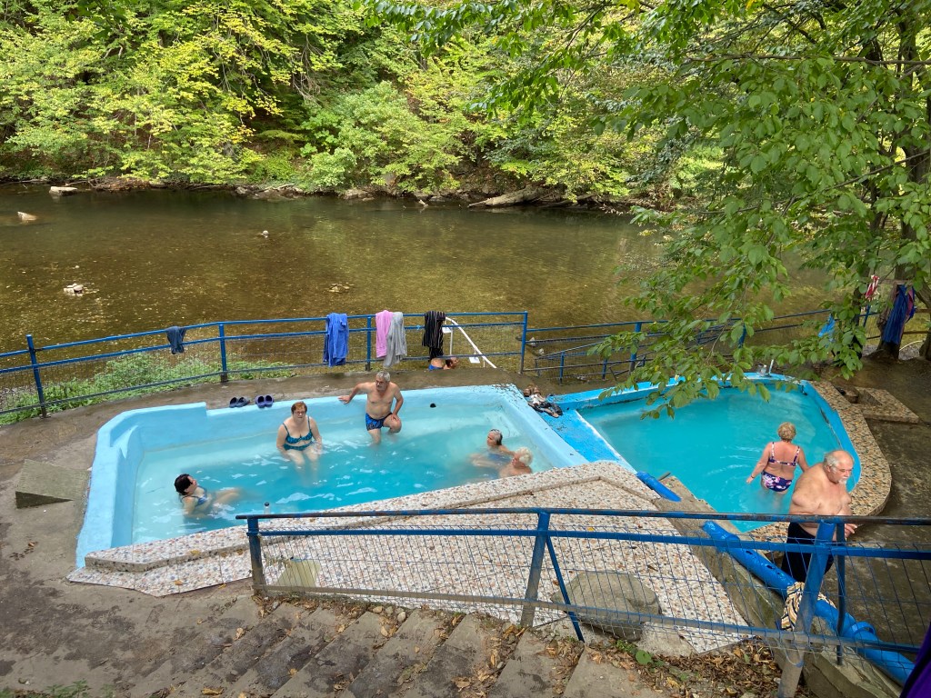 People relaxing in thermal water which is collected into a blue pool which is by the river side. 