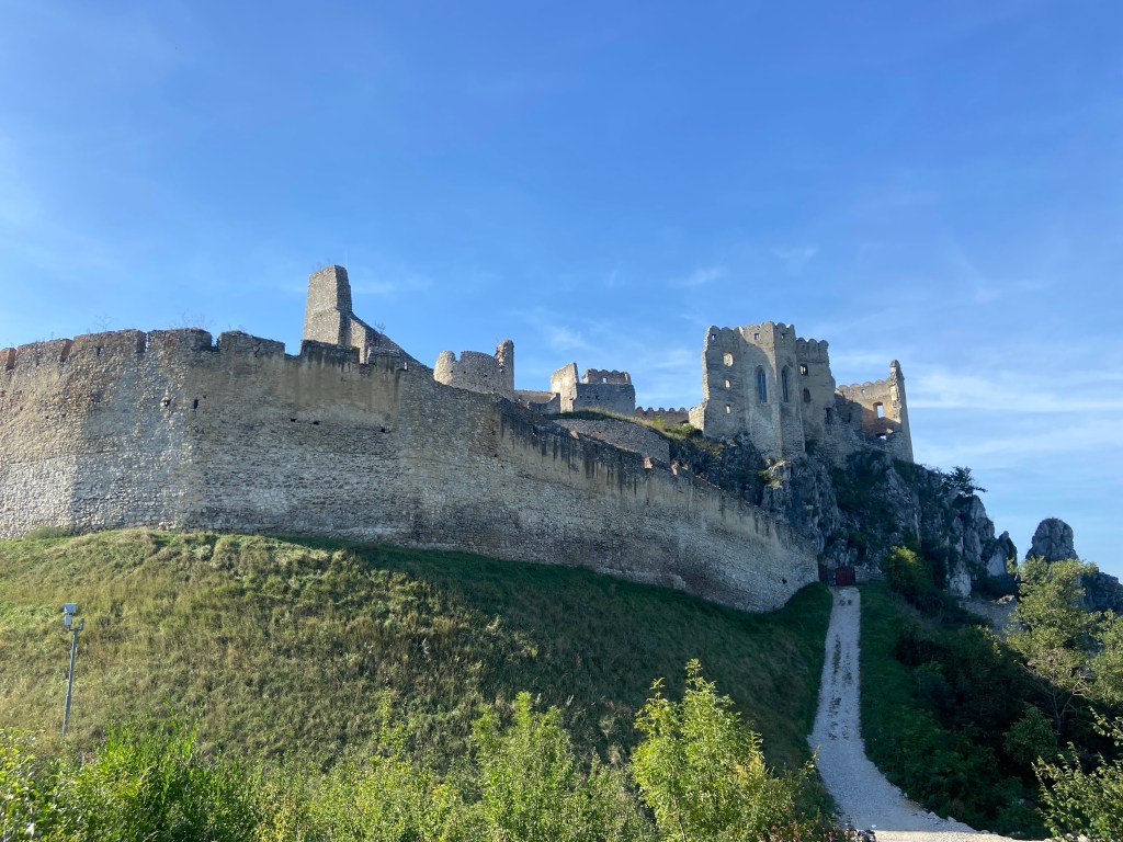 Partially ruined old stone castle fortress complex with an intact tall and imposing wall surrounding the ruin. 