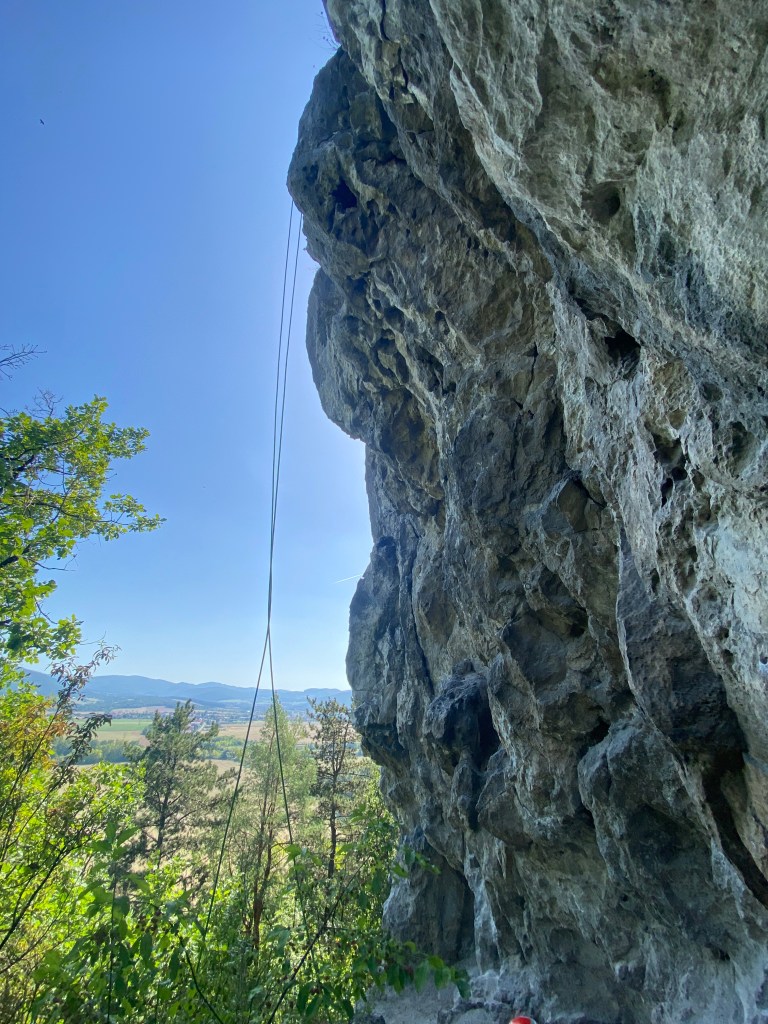 Overhanging white dolomite crag with darker features. There is a green rope hanging down from the top of the crag. which emphasises the steepness of the crag. 