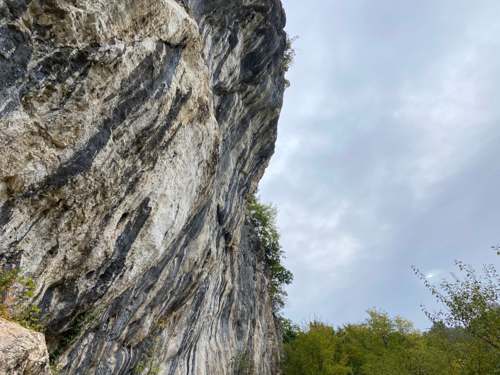 Imposing and overhanging limestone wall which has a steeper bulge at the top. The wall has many bumpy features and tufas   