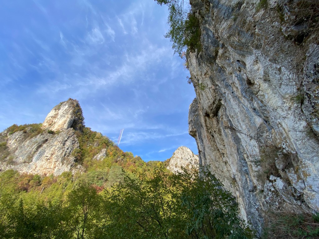 Limestone buttresses which protrude across the forested hillside which is stark white and blue. Across the valley hangs a large but worned Serbian flag. 