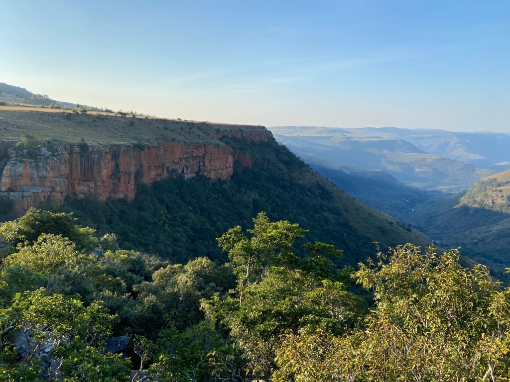 Mountain plateau with a long, orange band of cliffs and lush green mountains in the background. 