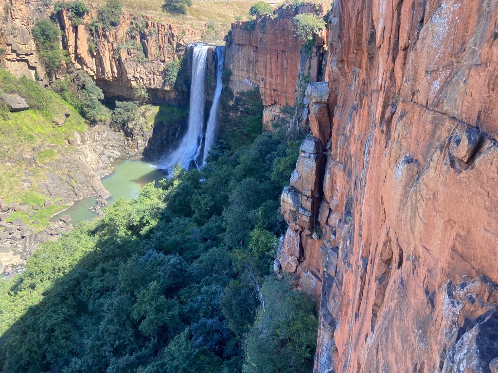 Large band of orange quartzite rock with a waterfall cascading off the top plunging down into the river below. 