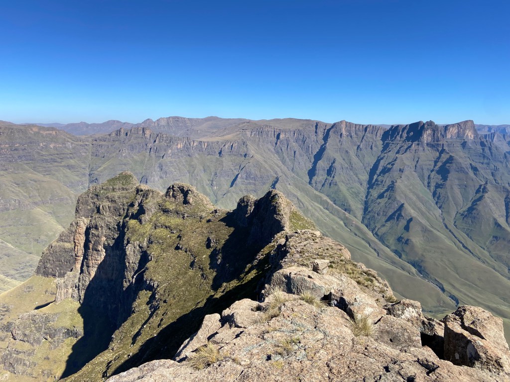 Rocky summit with a mountain plateau in the distance with steep, lush green sides. 
