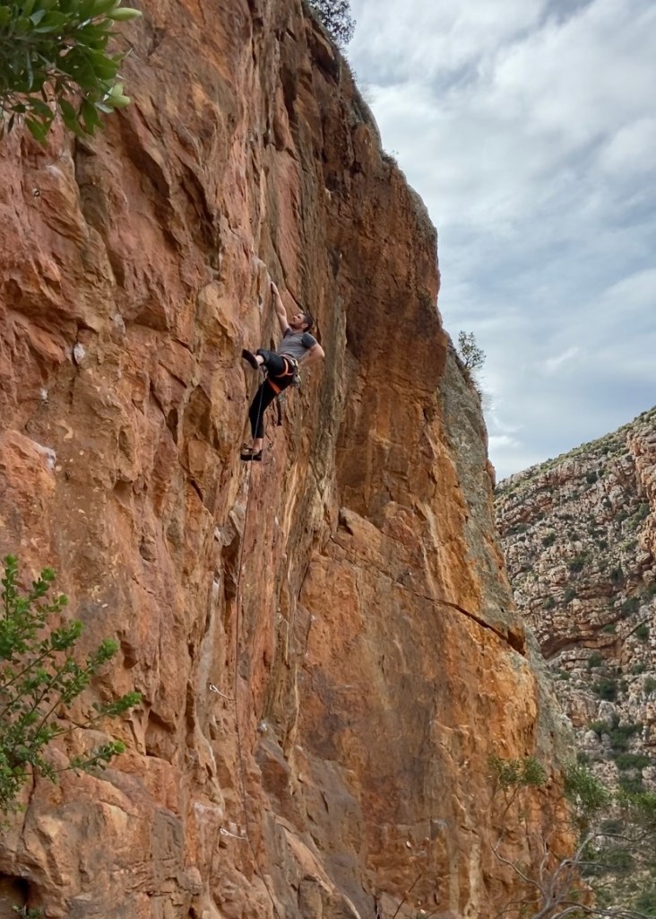 Climber chalking up on steep orange rock on an overcast day. 