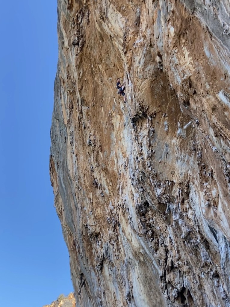 Climber navigating steep limestone tufas against a blue sky.