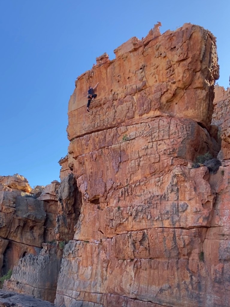 Climber on large orange sandstone pillar with large chicken head features. 