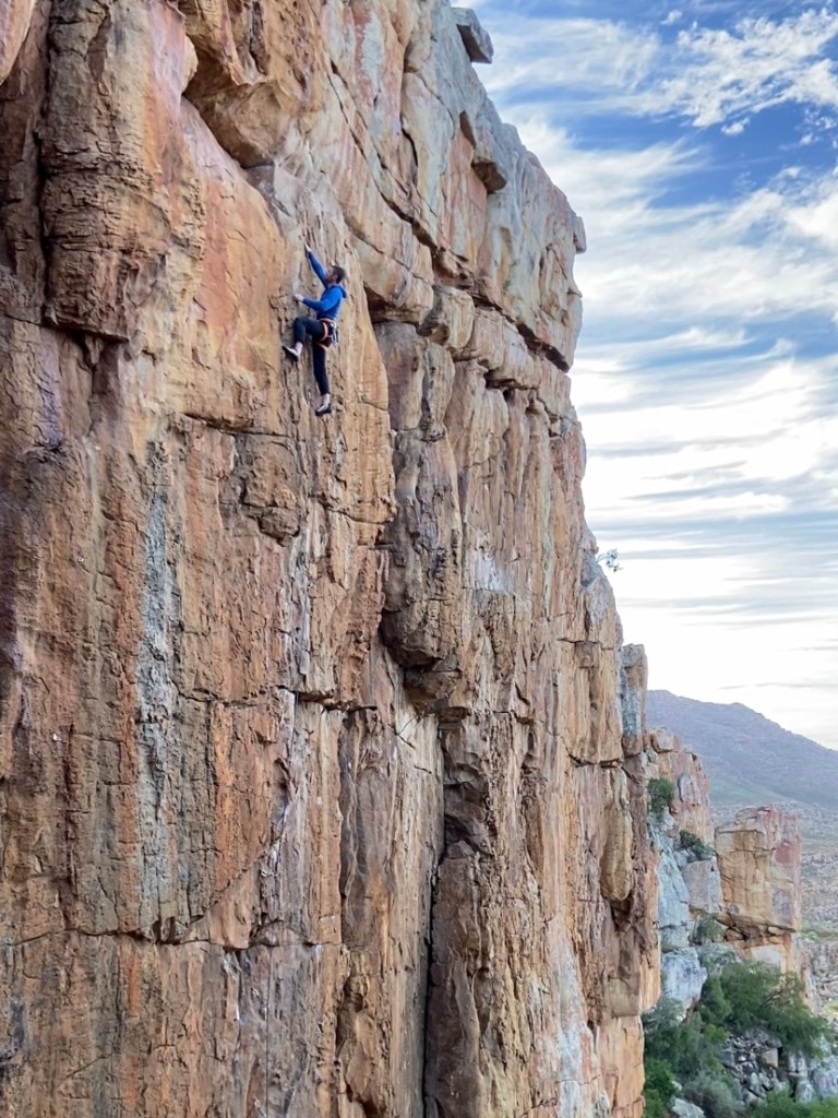 Climber on orange sandstone wall with horizontal and vertical cracks. 