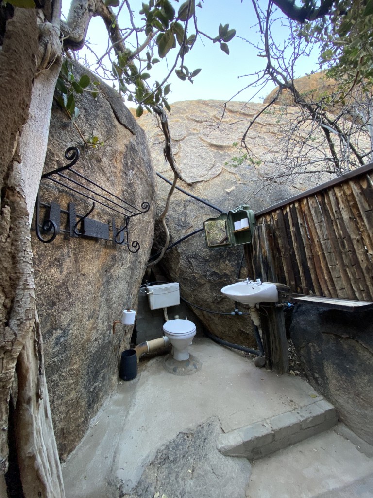 Toilet and sink set privately within some large boulders.