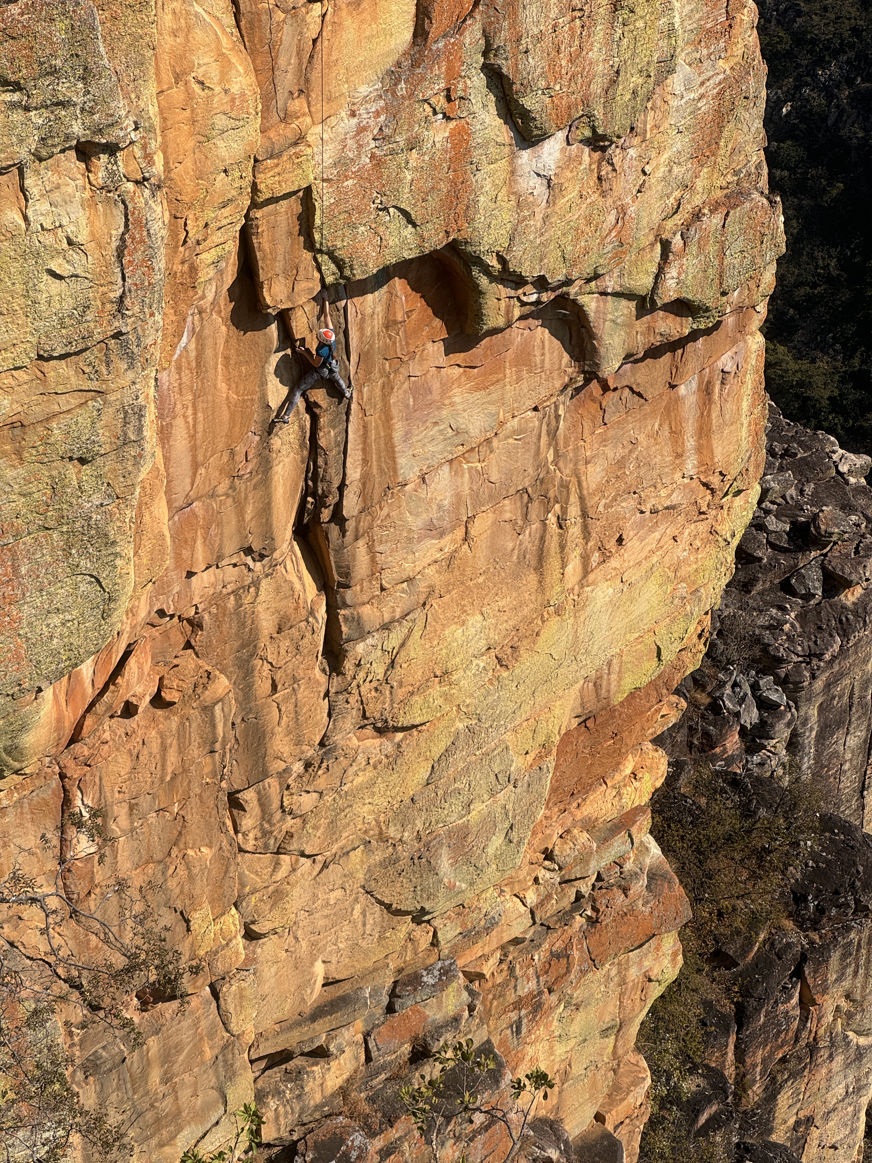 Climber making their way up crack systems on bright orange quartzite sandstone cliff.