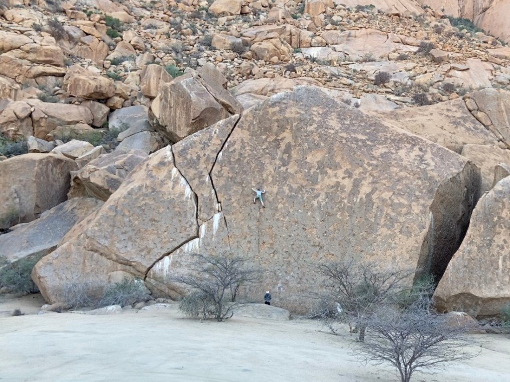 Climber on a giant boulder with crack features among a large boulder field.