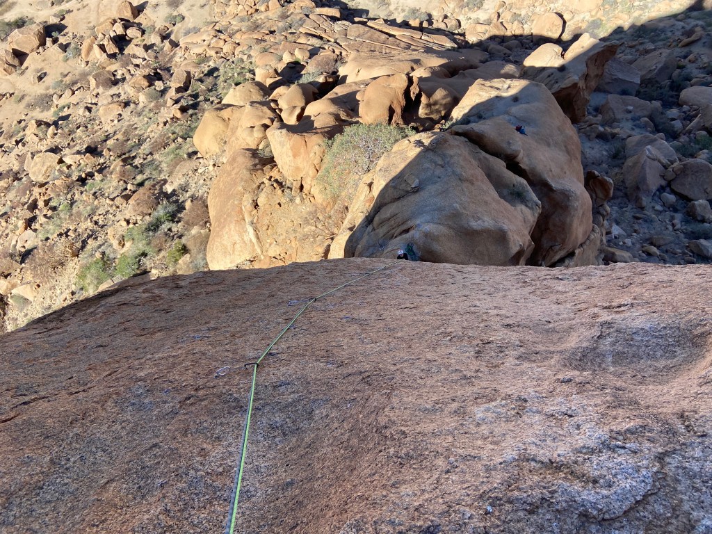 Looking downwards from a freestanding rock pinnacle to the belayer below and the boulders beneath.