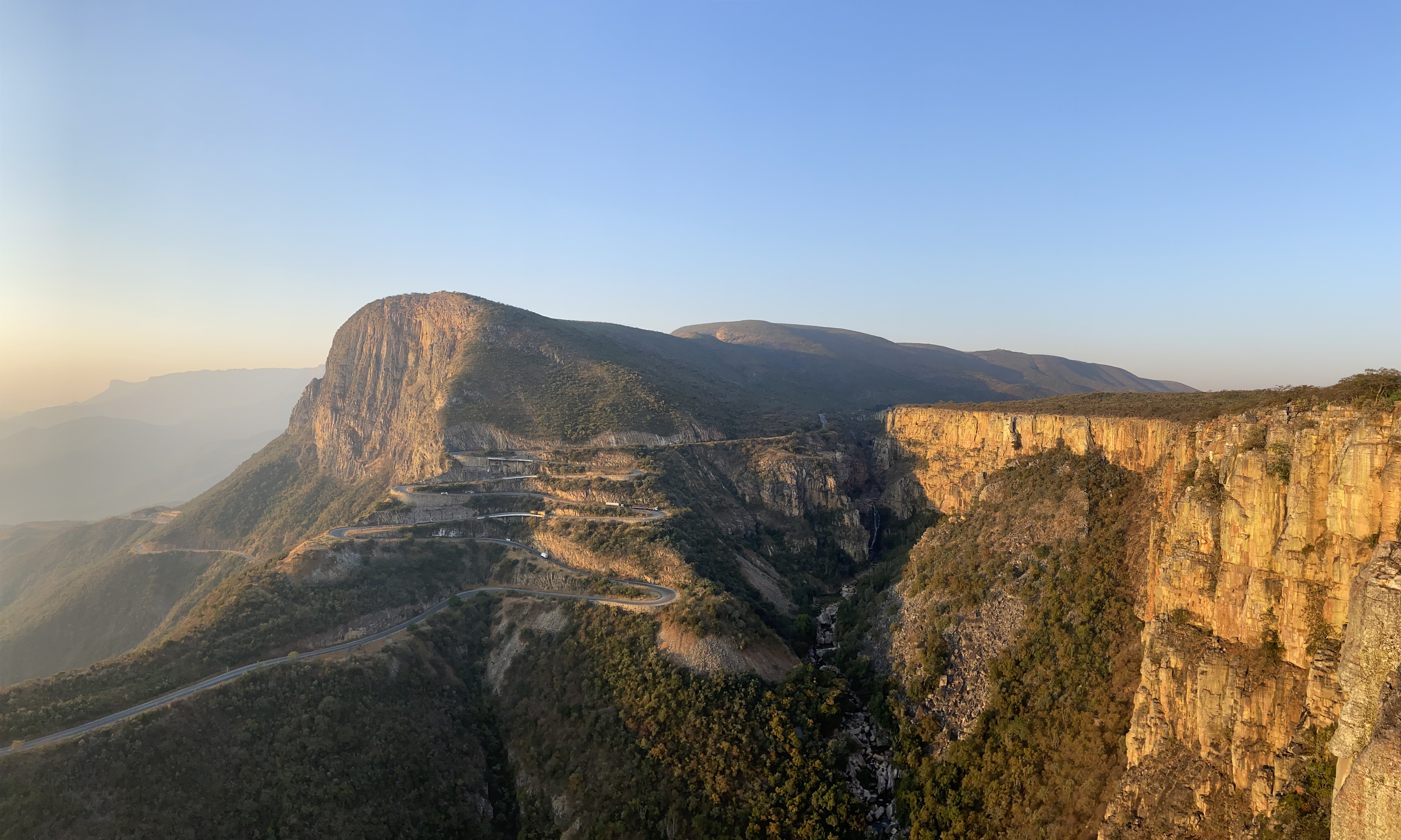 Dramatic serpentine road switching up a steep forested hill side with a deep ravine below.