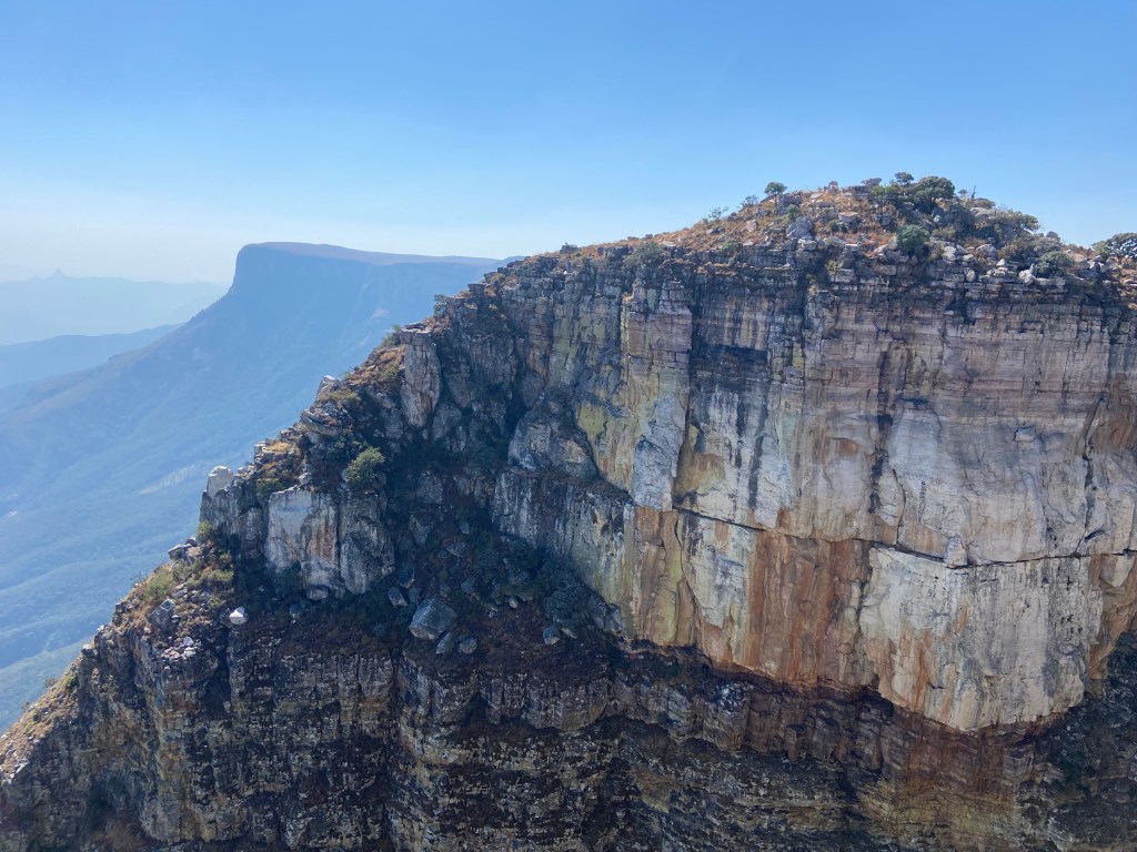 White and yellow quartzite sandstone cliff face with a plateau in the distance and vast Namibe plains below.